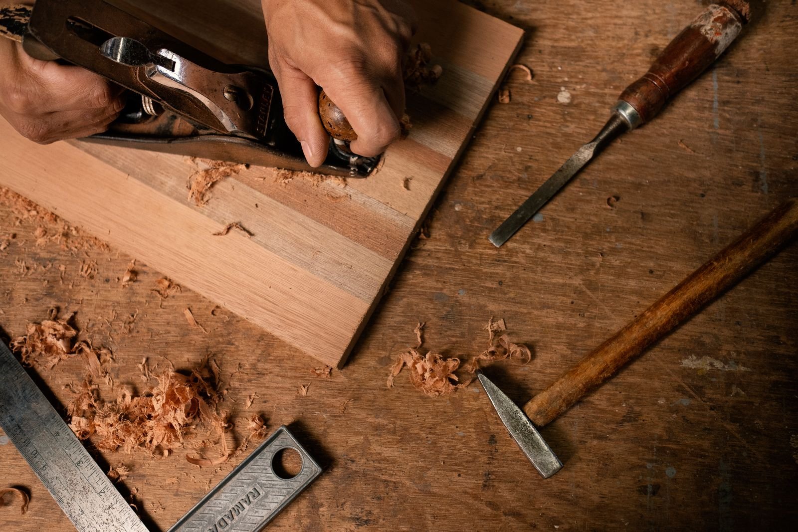มือช่างไม้ใช้กบไสไม้บนโต๊ะงาน พร้อมสิ่วและขี้กบ สำหรับงาน DIY ชั้นแมวติดผนัง